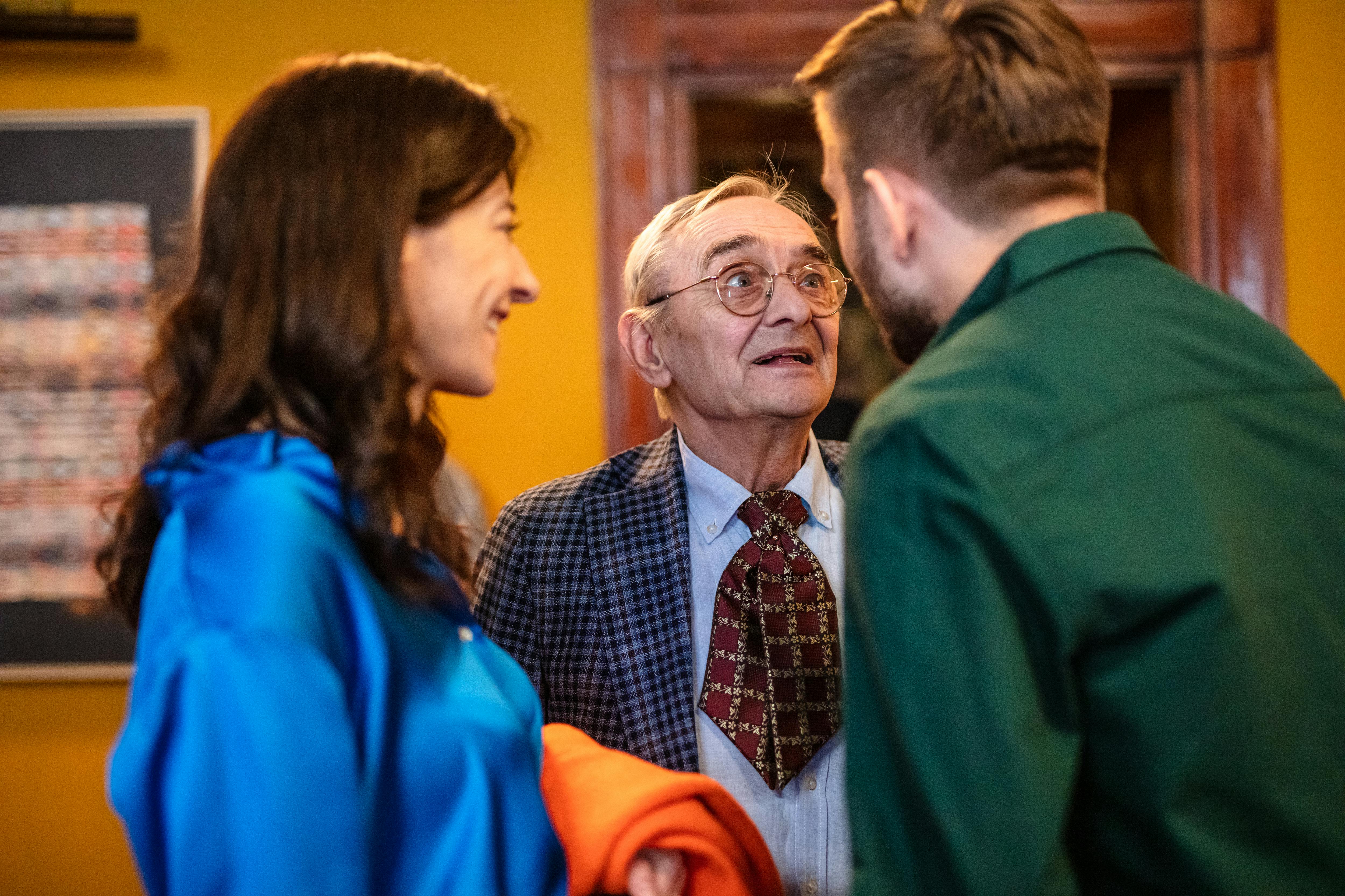 photo of an elderly man in glasses talking to two young people