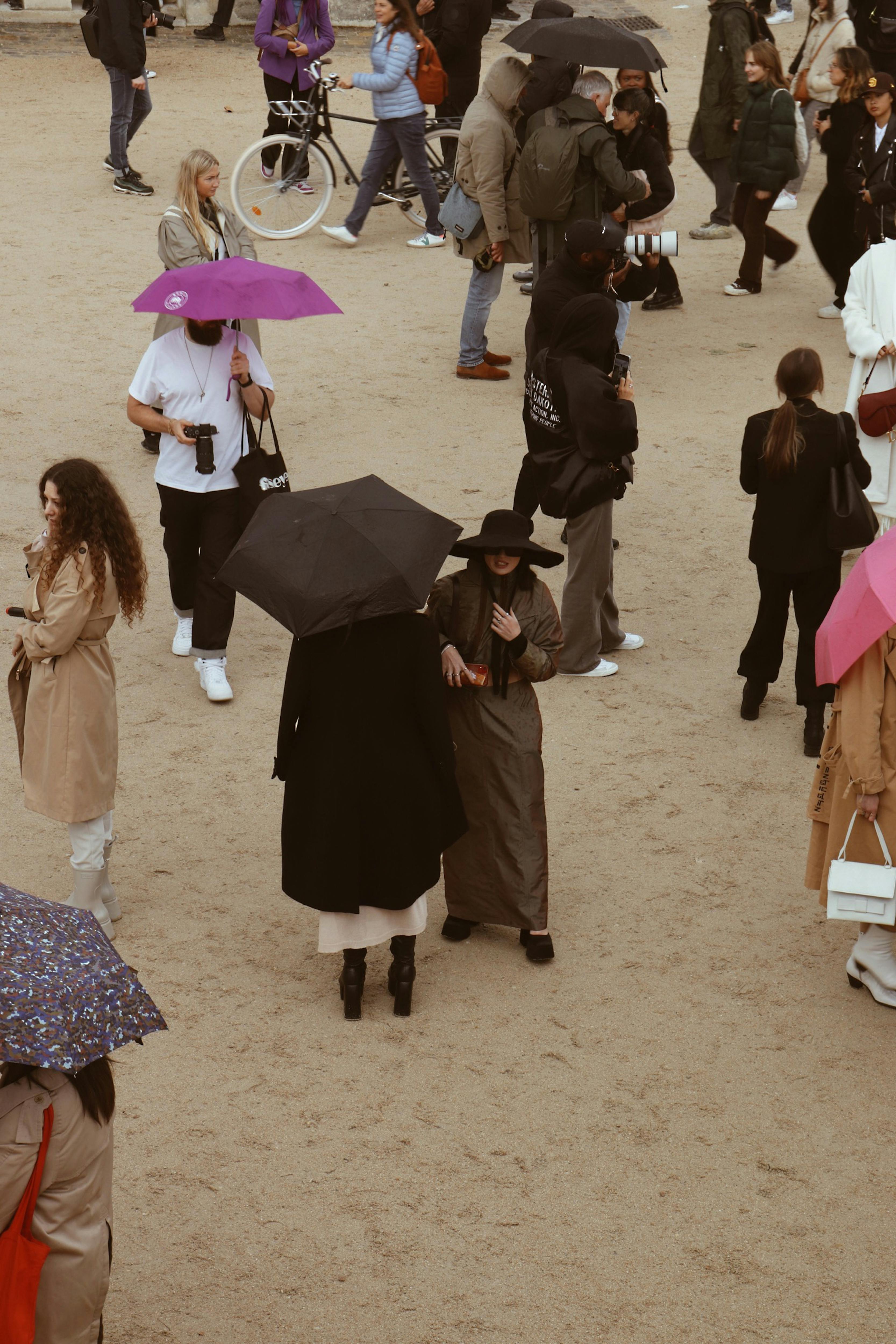 woman in black dress holding umbrella walking on brown sand