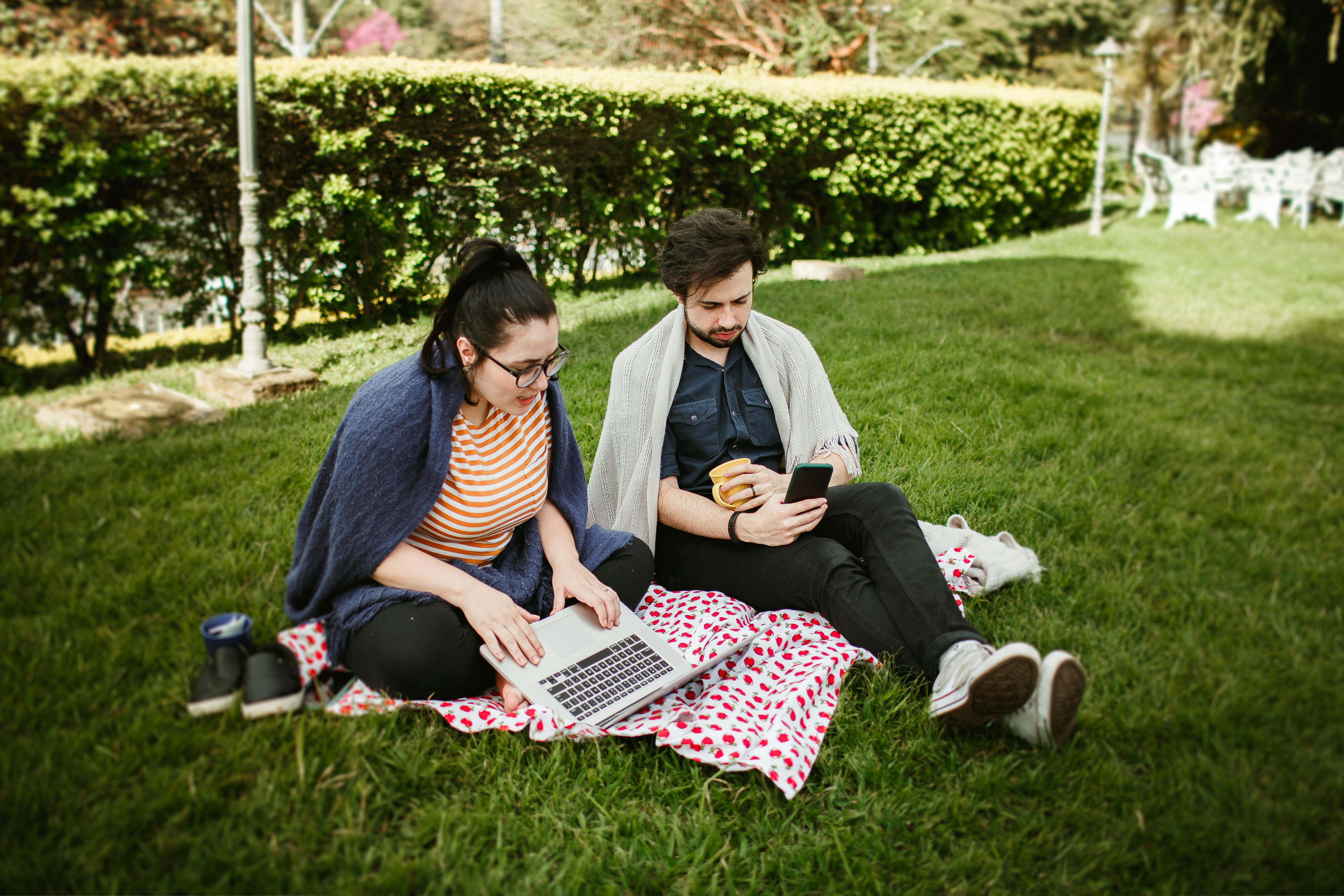 couple sitting with laptop and smartphone at picnic