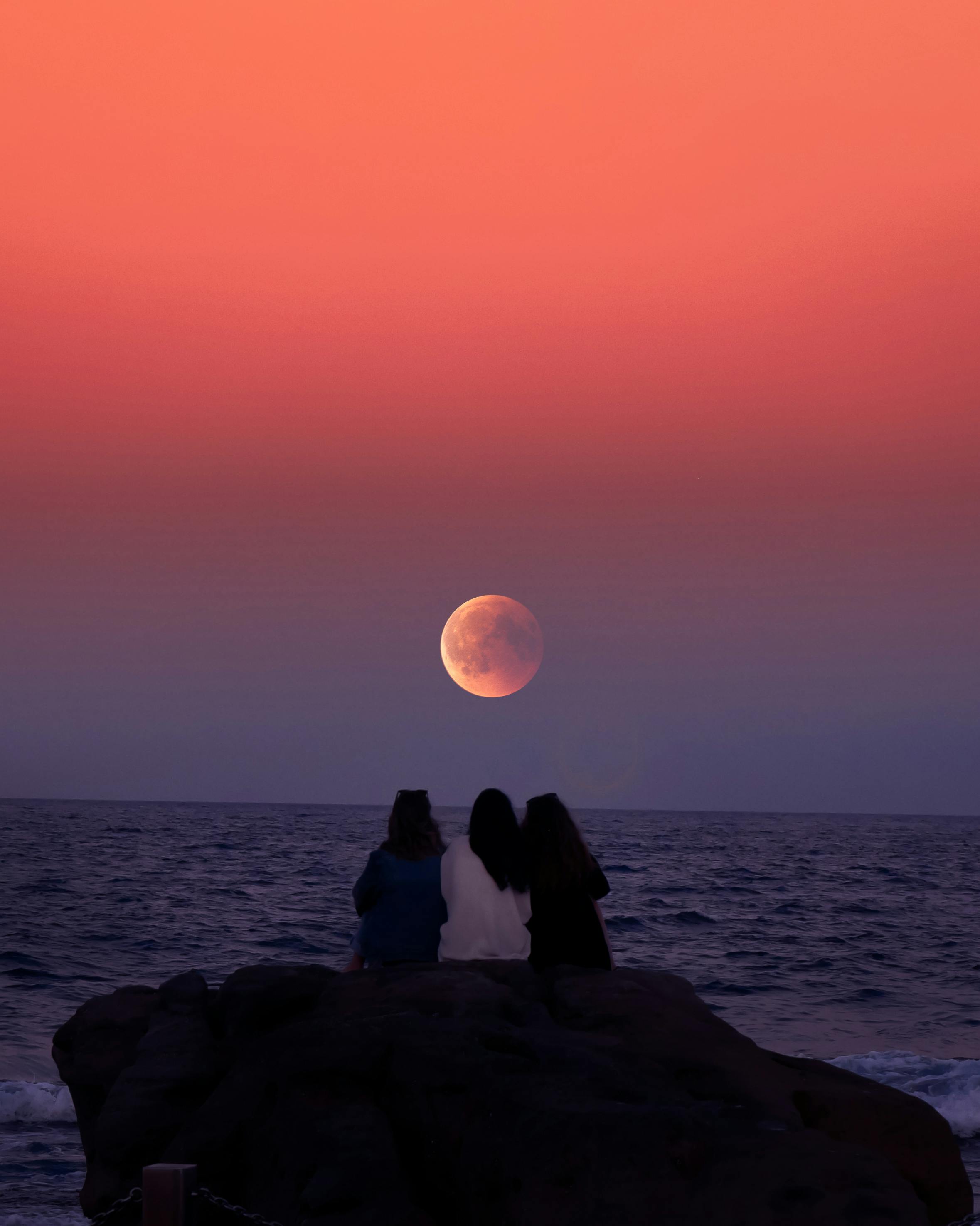 women sitting on rock infront of ocean