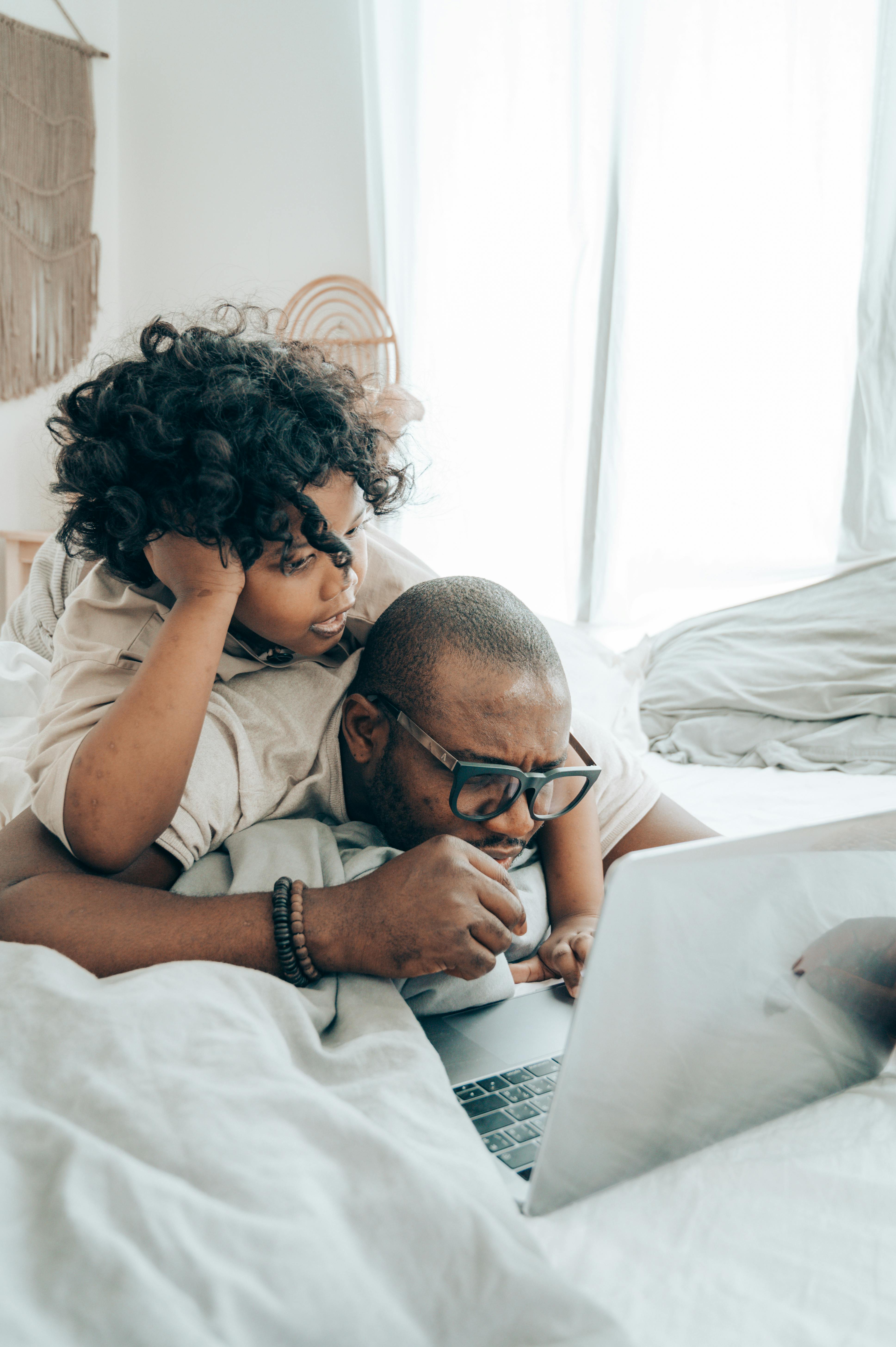 serious ethnic man and child with laptop in bedroom