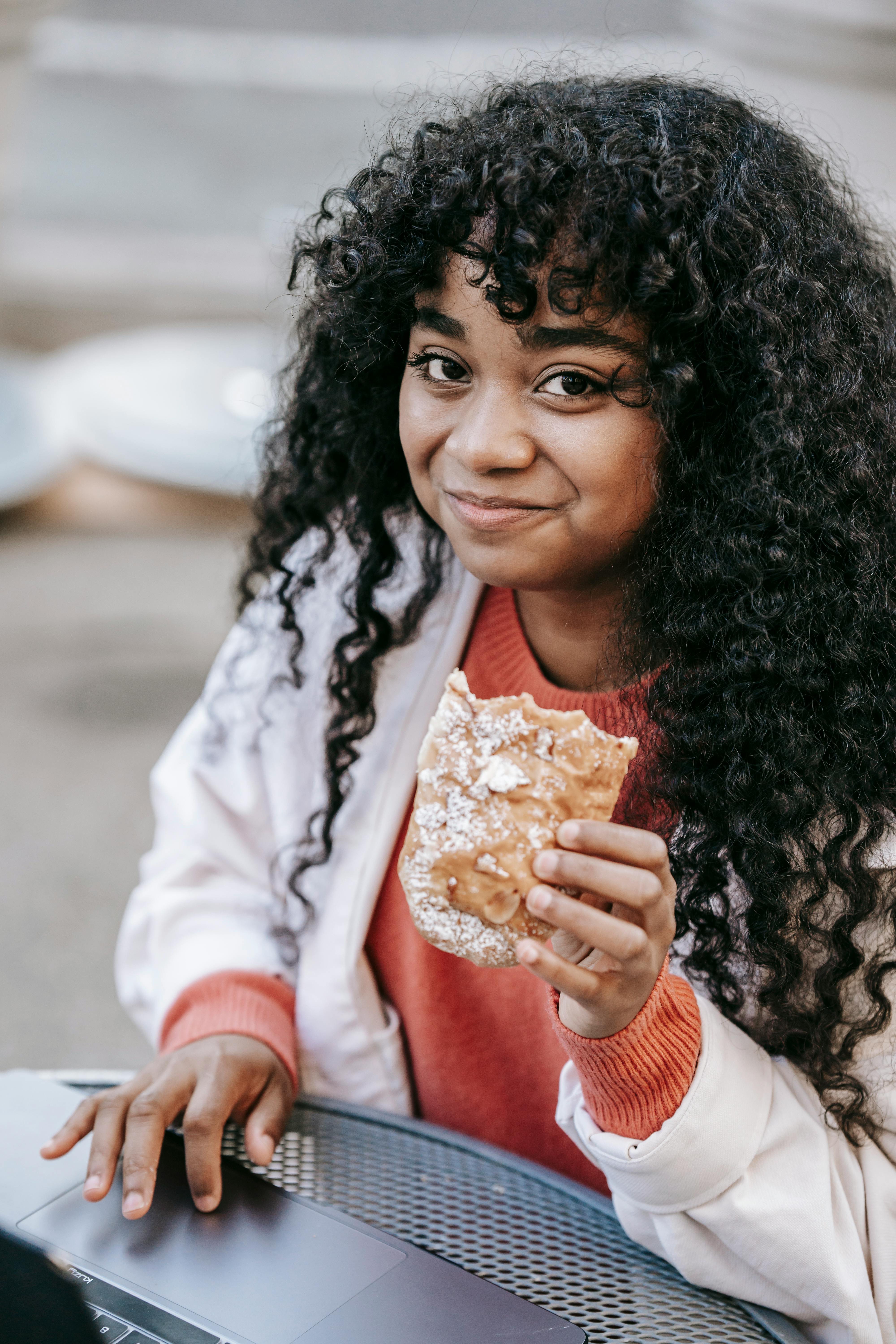 black woman using laptop and eating sandwich in street cafe