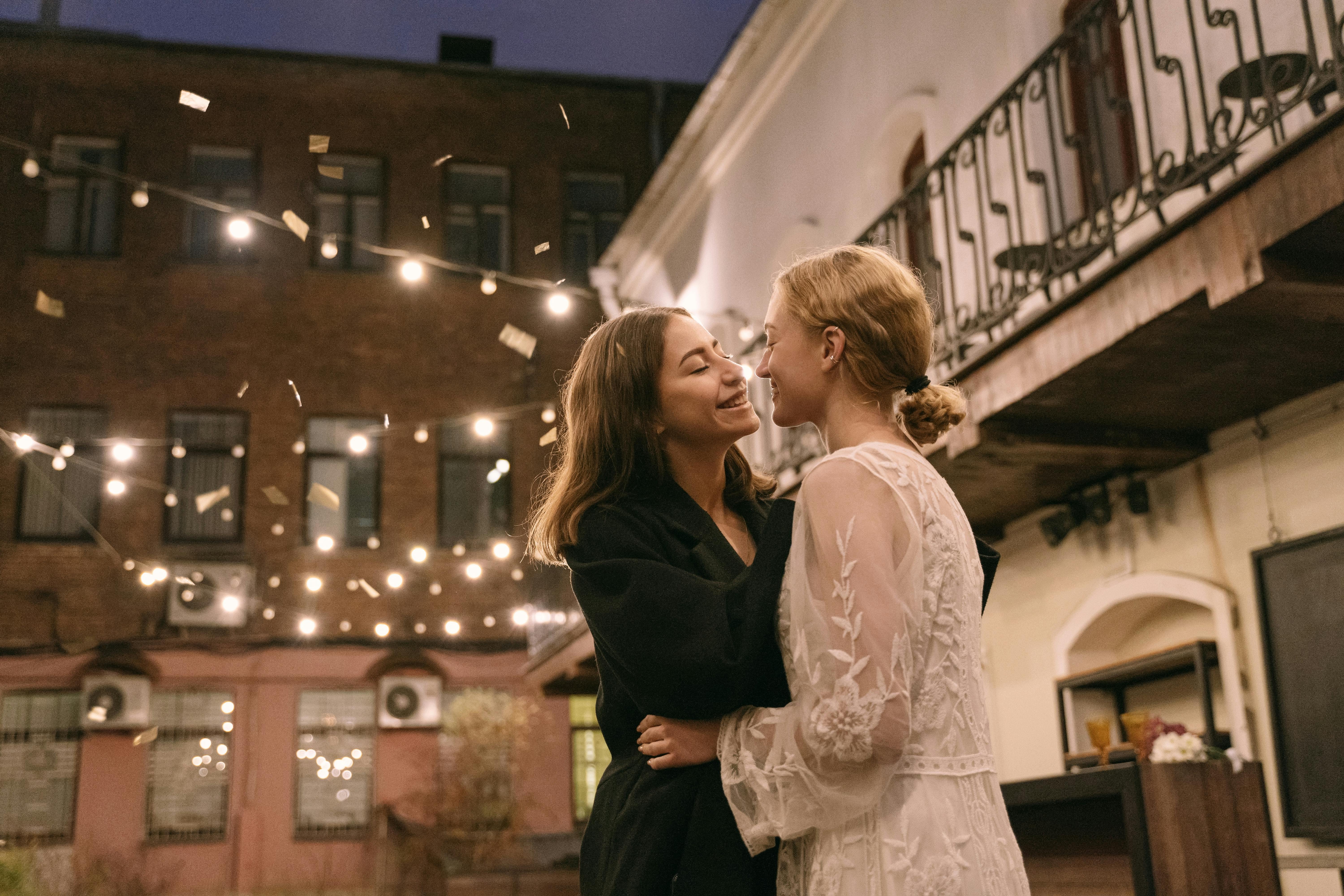 woman in black long sleeve shirt kissing woman in white floral dress