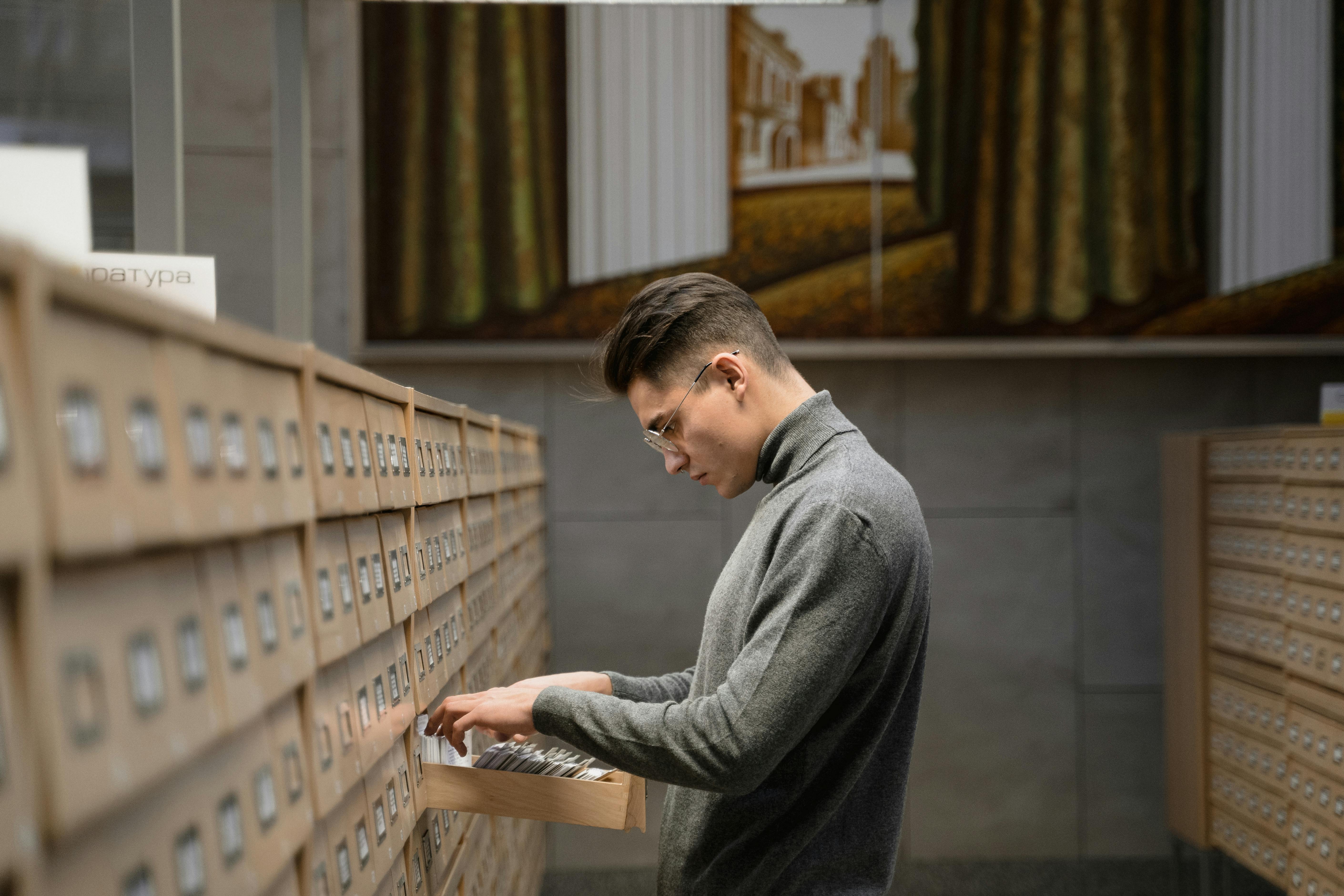 a man in gray sweatshirt looking at the records in a drawer