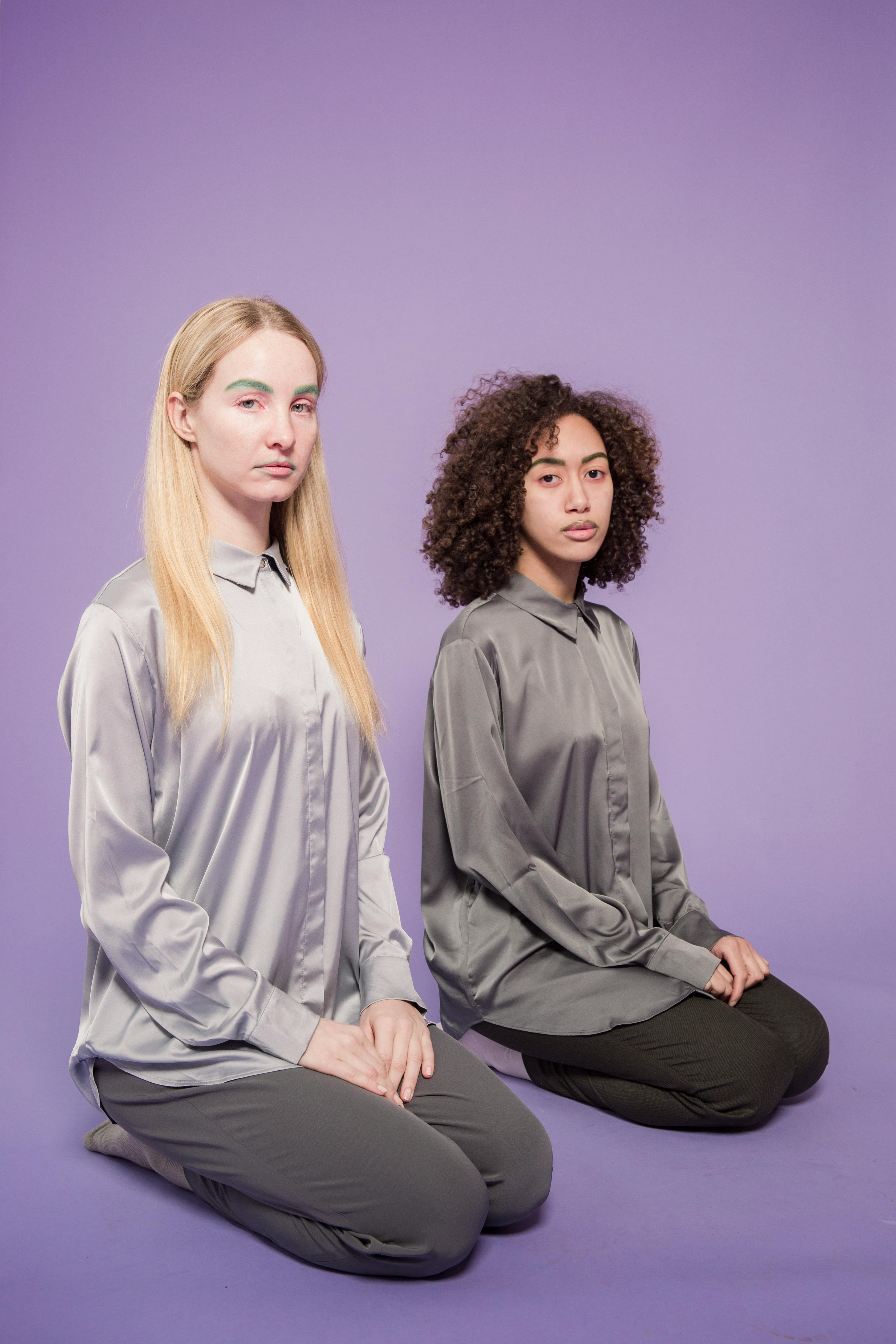 unemotional multiethnic women sitting on knees in studio