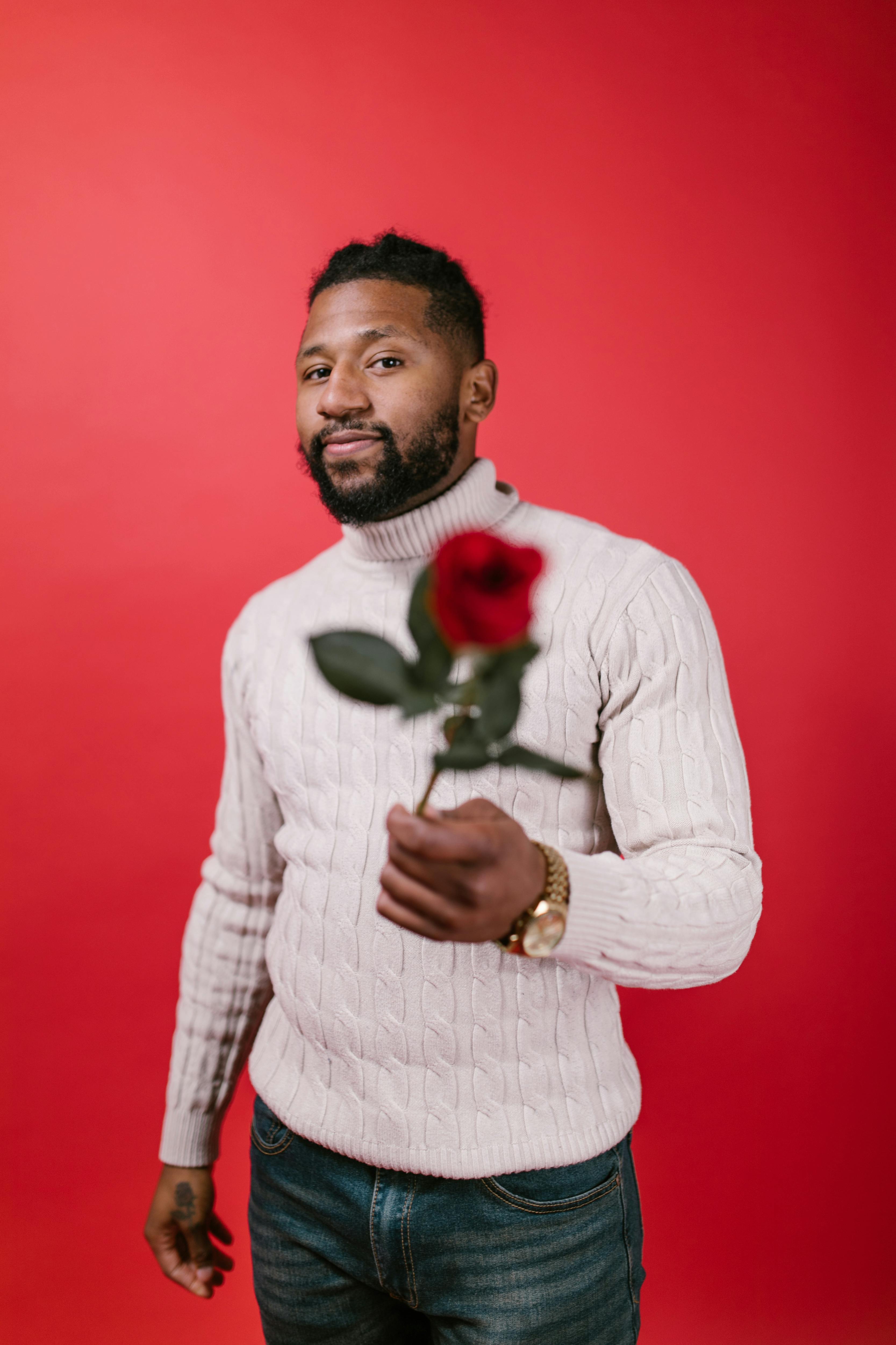 man in white sweater holding a red rose