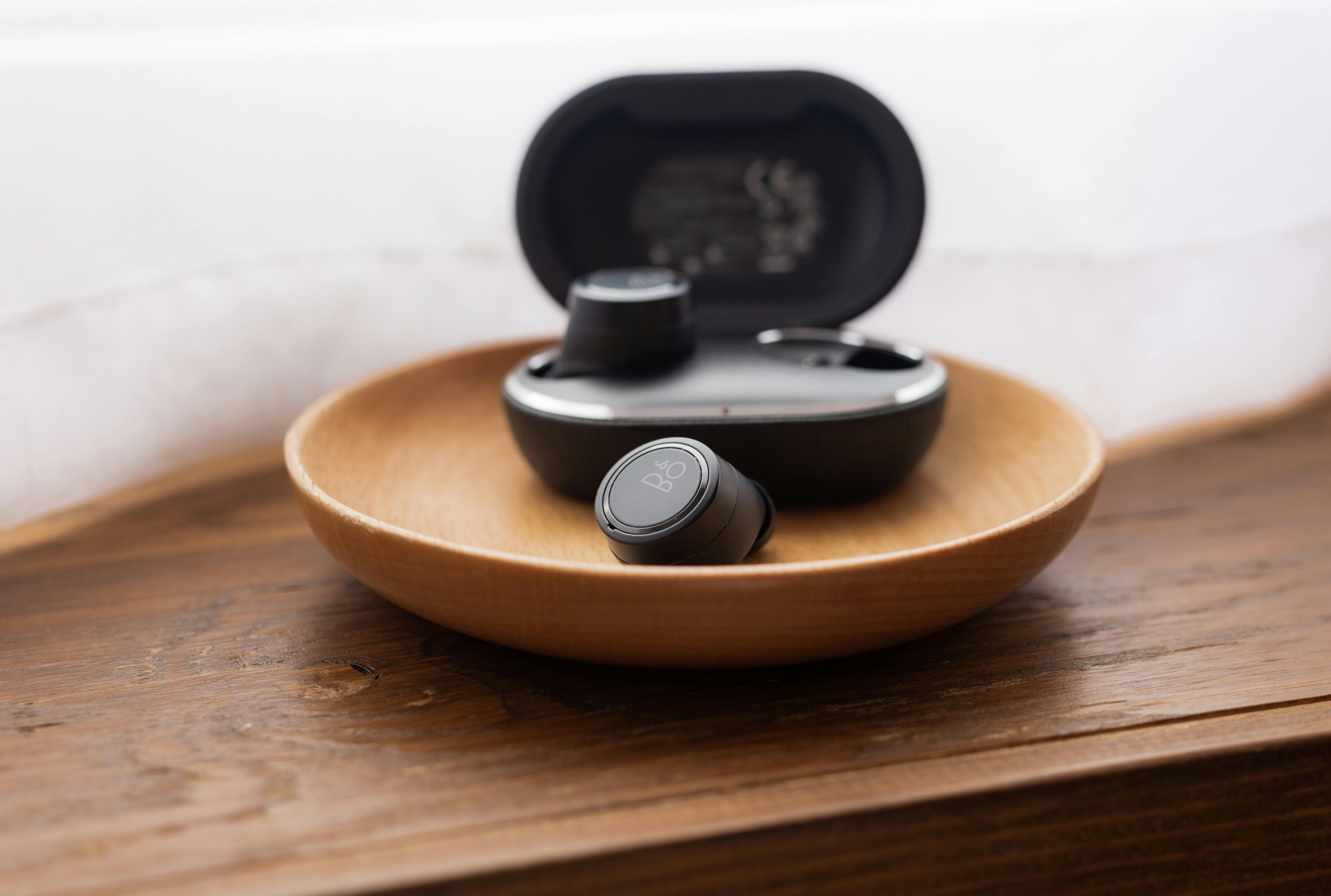 black wireless earphones with case in a wooden bowl