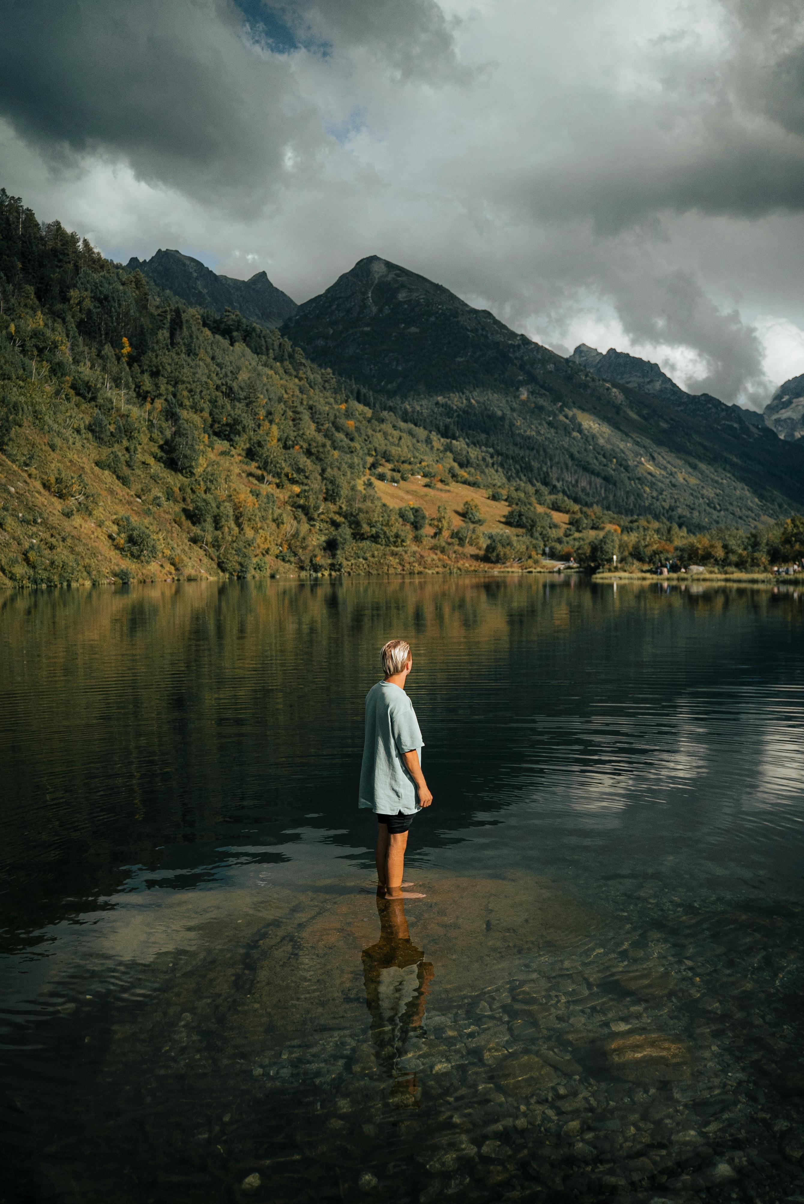 a person standing on shallow water and looking at mountains