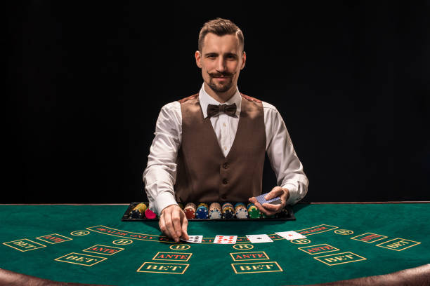 Portrait of a croupier is holding playing cards, gambling chips on table. Black background Portrait of a croupier is holding playing cards, gambling chips on table. Black background. A young male croupier in a shirt, waistcoat and bow tie is waiting for you at the blackjack table casino stock pictures, royalty-free photos & images